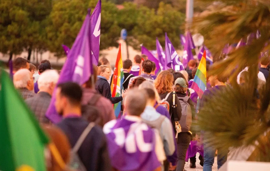 Volt Malta supporters marching with purple flags and a pride flag at a political rally.